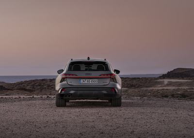 Rear view of the Audi A6 allroad (pearl grey) with a continuous light strip in a barren coastal landscape.