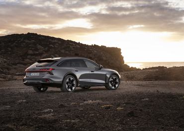 Three-quarter rear view of the Audi A6 allroad (pearl grey) against a coastal backdrop in backlight.