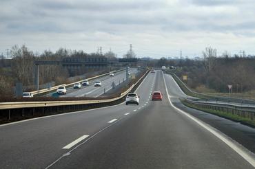 Several cars are traveling along a multi-lane highway under a cloudy sky, creating a sense of movement and journey. The scene captures a typical travel experience.