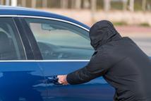 Unknown hooded man attempting to open parked car door theft crime risk and vehicle security problem concept urban safety and insurance theme