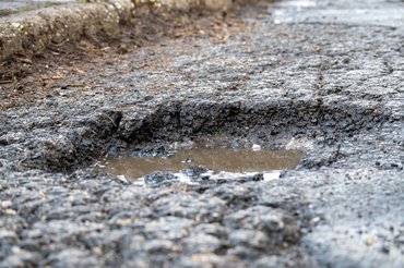 Close-up of potholes on a wet urban road with a passing vehicle, illustrating damaged infrastructure, poor road conditions, traffic safety risks, and the need for road maintenance in city environments.