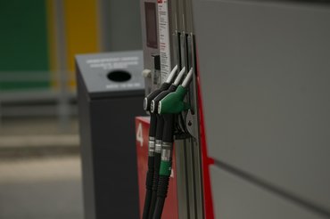 Fuel pump nozzles at urban station green and black hoses resting on metal dispenser beside trash bin, concrete forecourt and payment terminal, city