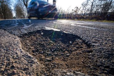 PRODUCTION - 09 March 2026, Mecklenburg-Western Pomerania, Lützow: A car drives past a pothole in a district road. Prolonged frost and repeated freeze/thaw cycles have taken their toll on the roads in Mecklenburg-Vorpommern. Photo: Jens Büttner/dpa (Photo by Jens Büttner/picture alliance via Getty Images)