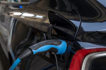 Close-Up Of Electric Vehicle Charging Plug Connected To Urban EV Charger Station With Blue Cable