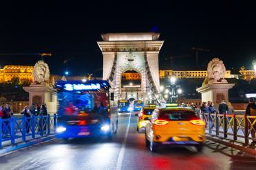 Budapest, Hungary - November 7, 2025: Iconic Chain Bridge at night in Budapest with motion blurred bus and cars passing by the stone lion statue.