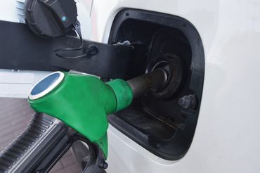 A green fuel nozzle inserted into the fuel tank of a white modern car